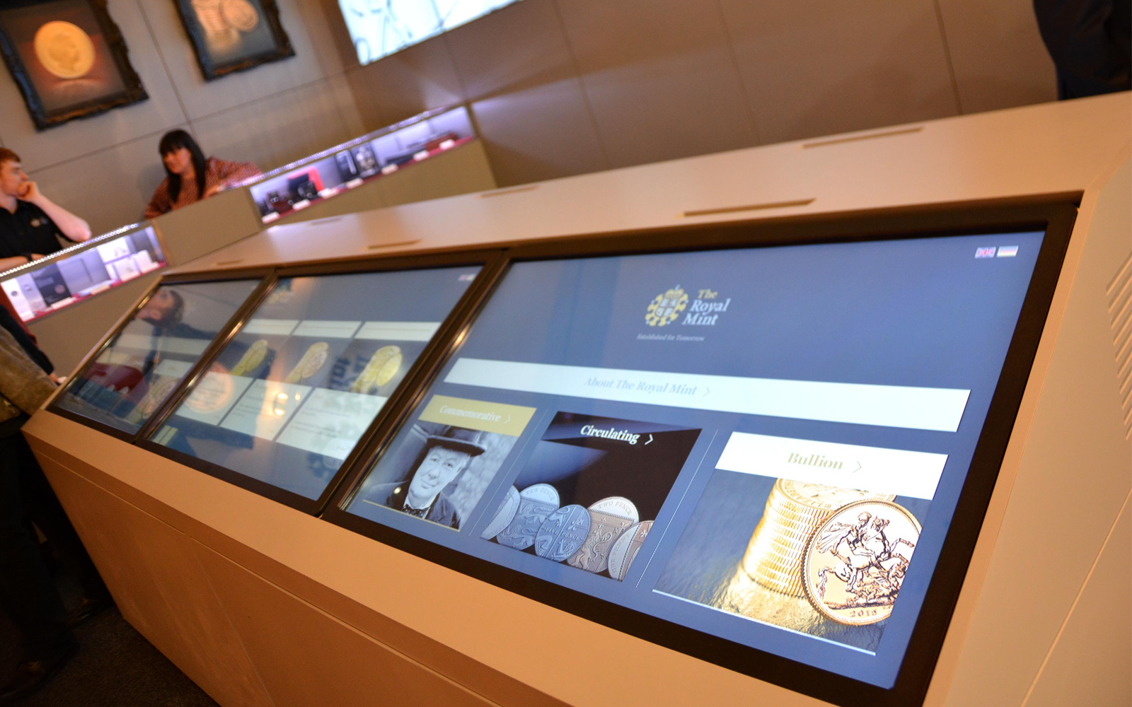 man and women interacting with The Royal Mint interactive touchscreen display software shown on large monitors