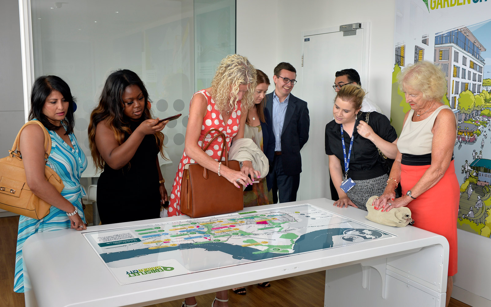 group of people smiling and interacting with ebbsfleet touchscreen display on white table in office